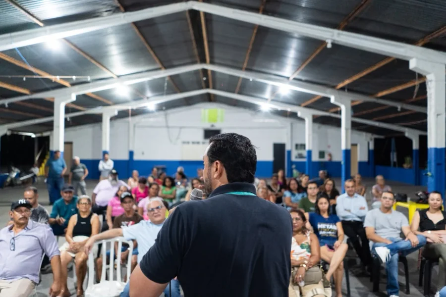 Allan Kardec fala ao microfone para moradores reunidos em um galpão